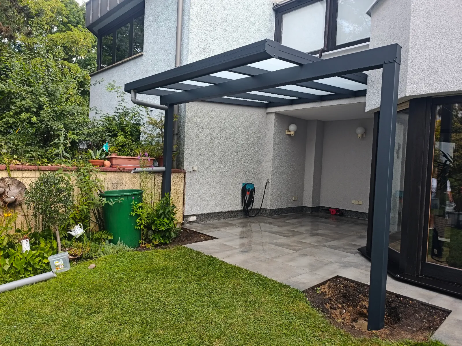 Schlankes anthrazitfarbenes Terrassendach an moderner Hausfassade